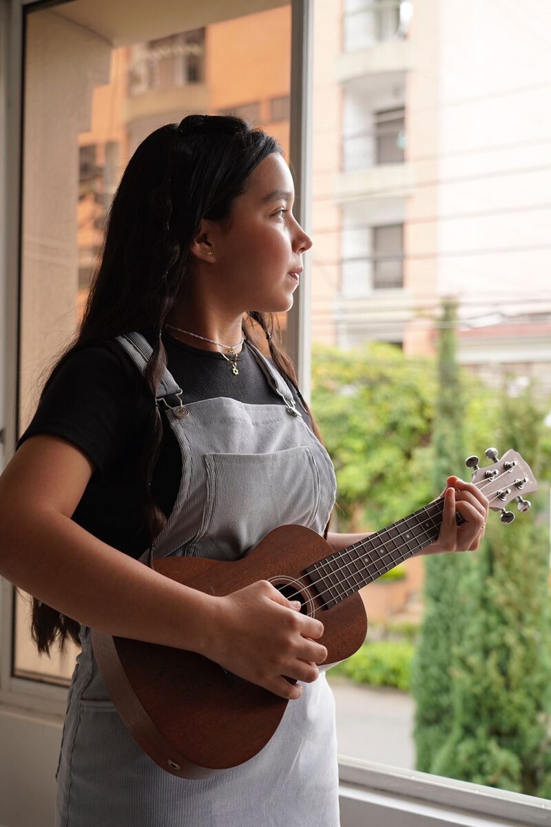 Joven tocando ukulele junto a una ventana